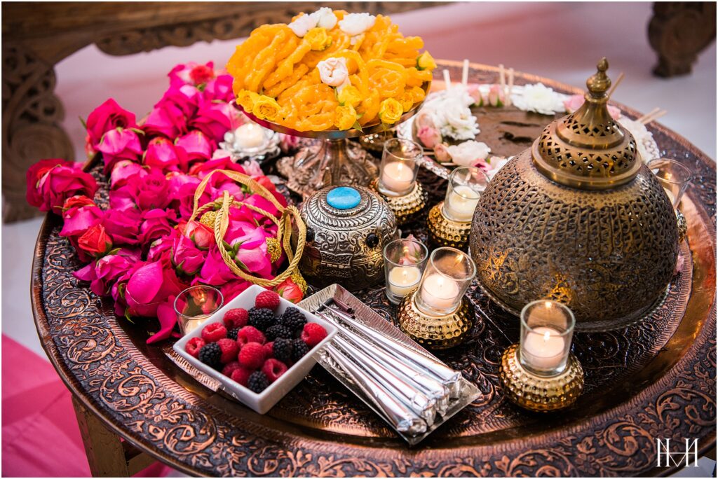 Mehndi, henna paste, flower garlands, candles, indian sweets and fruits displayed at the henna mehndi party
