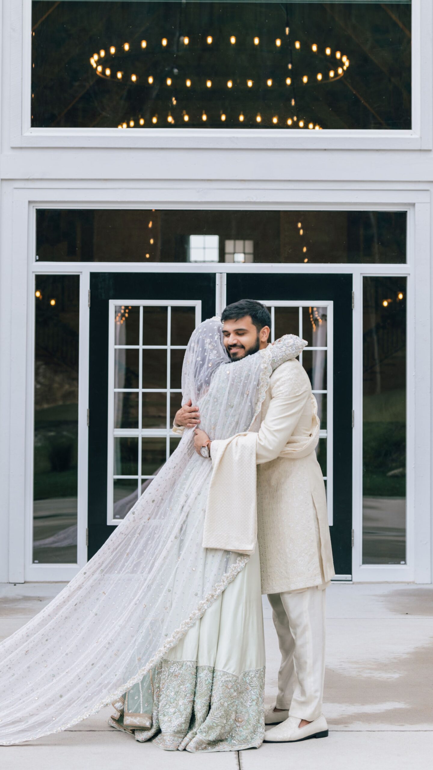 bride and groom hugging in front of white barn in Missouri